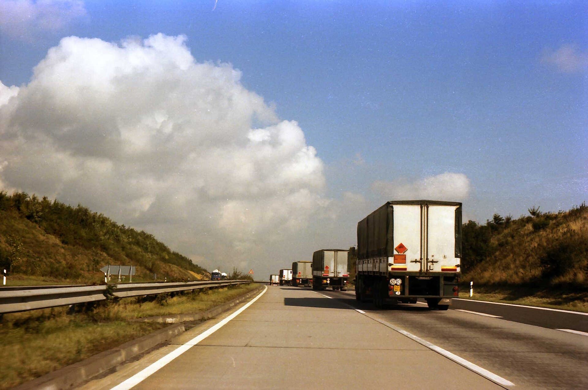 Schwarz-Weiß-Foto: eine Kolonne Lkw auf einer leeren Autobahn in der Eifel, darüber ein weiter Himmel.